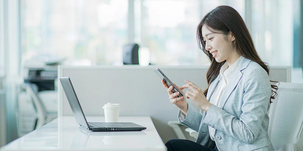 A woman at a desk looking at her phone, smiling at what she reads